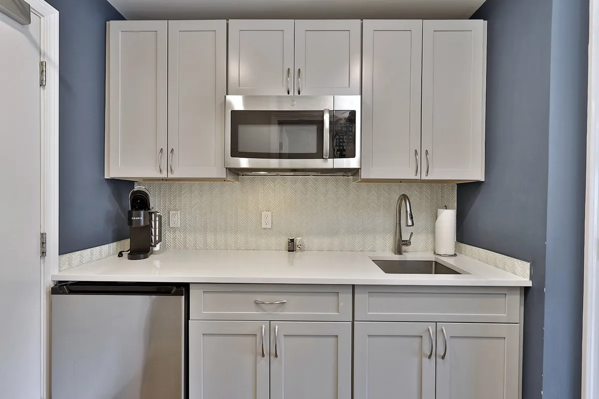 This image showcases a compact yet modern kitchenette area, featuring a microwave, sink, coffee machine, and cabinetry designed for efficiency and comfort. The scene is inviting and practical, suggesting easy preparation of snacks or small meals. The lighting and organization make the space feel both functional and welcoming, aligning perfectly with the description of 'effortless meal moments.'