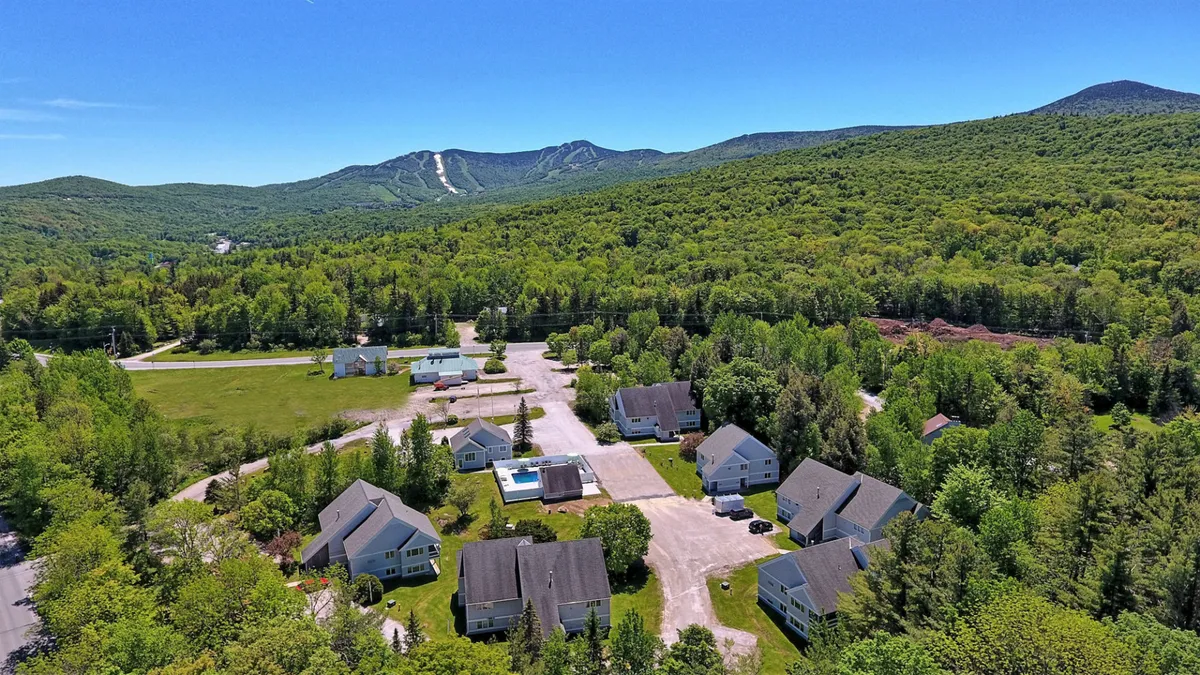 An inviting exterior view that captures a mountain range, a swimming pool area, clusters of houses, and lush greenery. The landscape highlights the property's location within a vibrant, activity-rich resort environment.