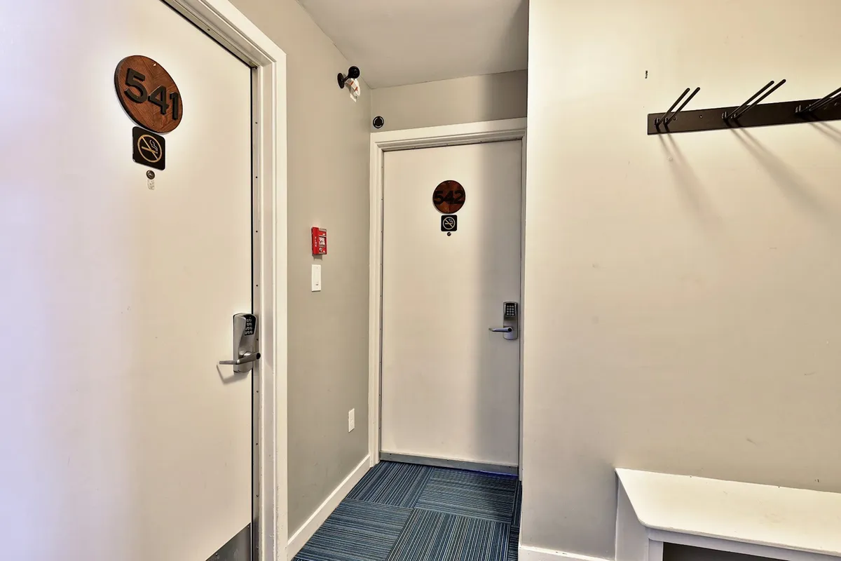 A welcoming hallway with room numbers on doors, a coat rack, and blue carpeting. The image captures the transition from the communal resort areas to the privacy of your renovated condo.