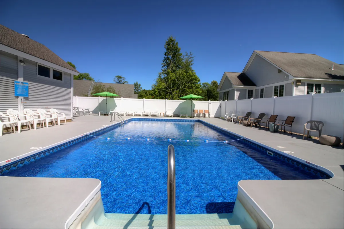 A serene pool scene with lounge chairs, green umbrellas, and a backdrop of verdant trees. The tranquil setting is ideal for quiet afternoons, reading by the water, or gathering with friends for a swim.