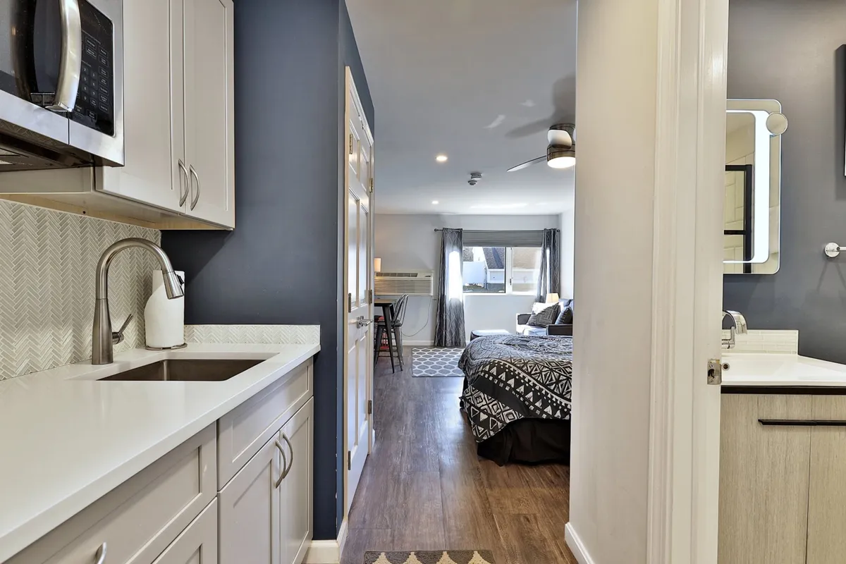 This image captures the in-room kitchenette with modern appliances, alongside a glimpse of the adjacent bedroom area. The kitchen space is well-equipped for quick meals or snacks, and the overall setting is cozy and inviting, perfect for guests seeking self-catering convenience during their stay.