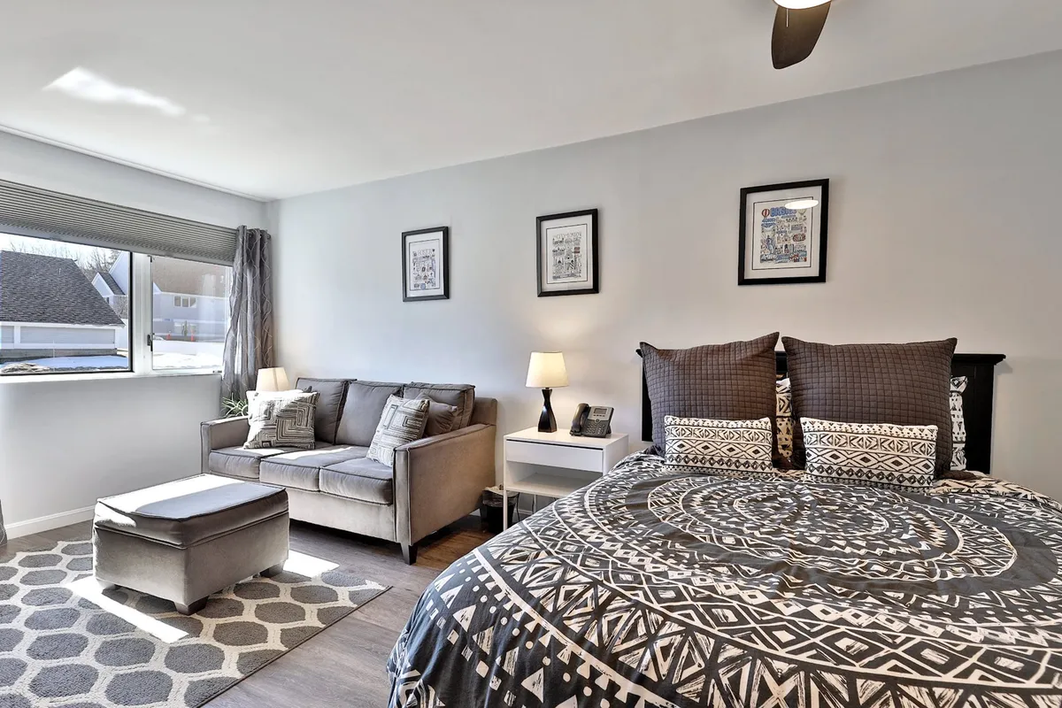 The image features a cozy living area with a bed dressed in patterned bedding, a comfortable sofa and ottoman, and framed artwork on the walls. Sunlight streams into the space, emphasizing a welcoming atmosphere suitable for relaxing between activities or before heading out to explore.